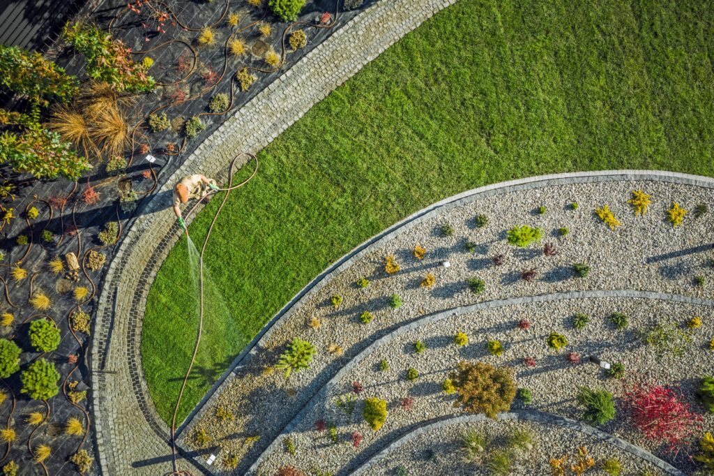 Building Backyard Garden. Landscaping and Gardening Industry. Caucasian Gardener with Hose Watering Newly Installed Natural Grass Turfs. Aerial Photo.